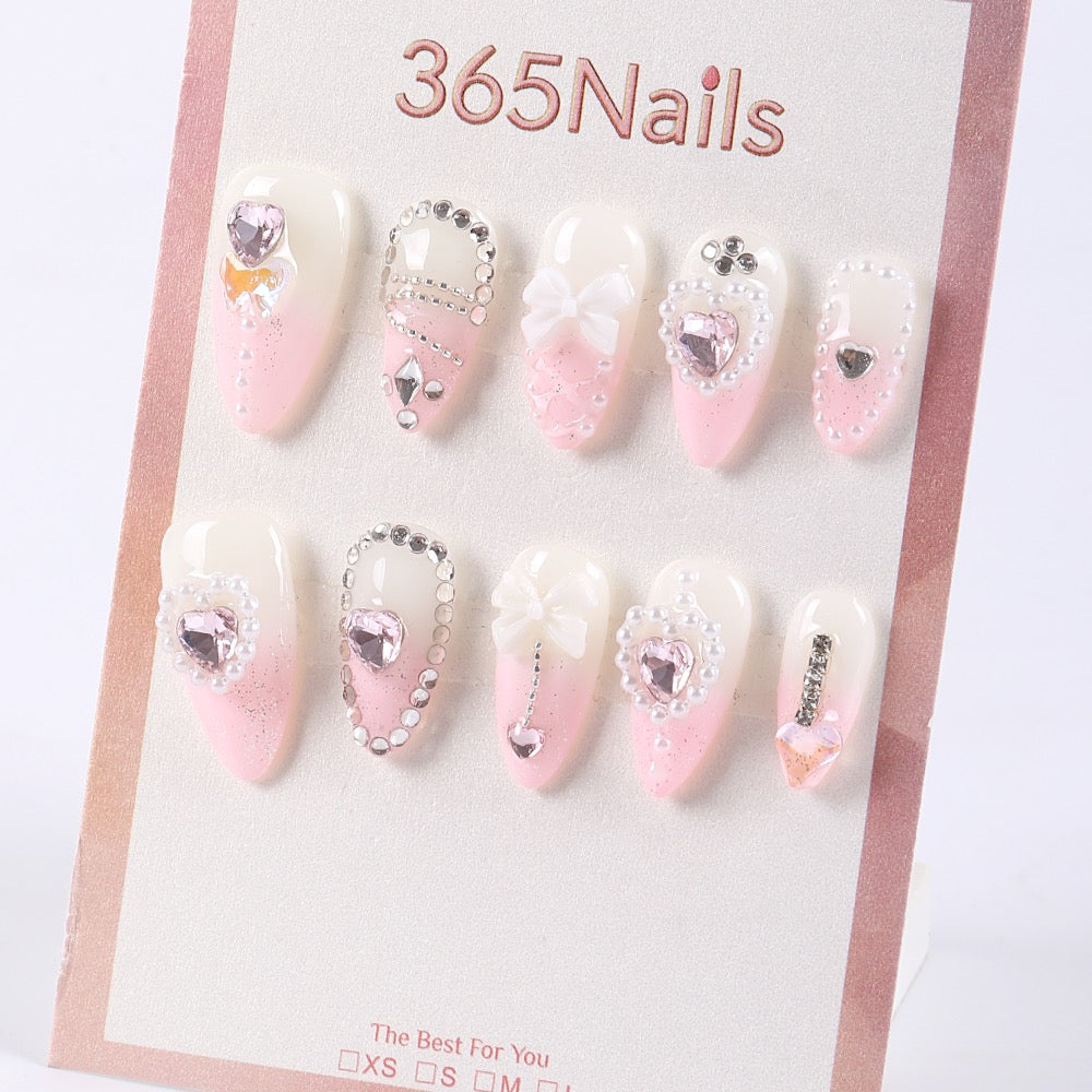 Uñas postizas 365Nails color blanco lechoso con degradado rosa bebé, corazones con ribete de perlas, pedrería y lazos 3D.
