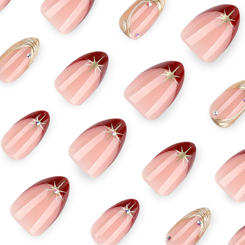 Close-up of nude almond nails with deep red tips and gold starburst rhinestones.