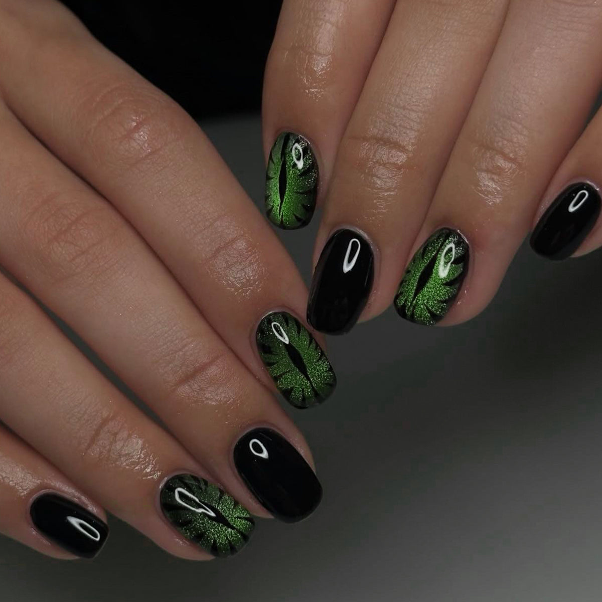 Hand wearing black and green cat-eye press-on nails with eye motif