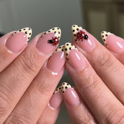 Hand wearing glossy pink almond press-on nails with cream french tips, black polka dots and a 3D ladybug charm