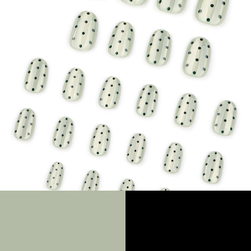 Multiple pale green polka dot press-on nails scattered on white background