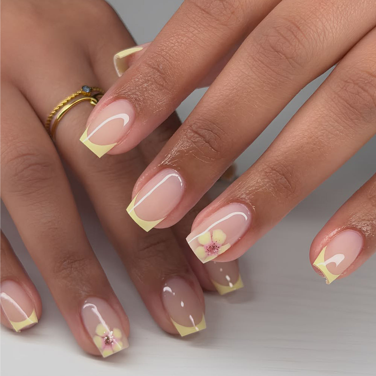 Hand wearing nude press-on nails with yellow french tips and small flower accents