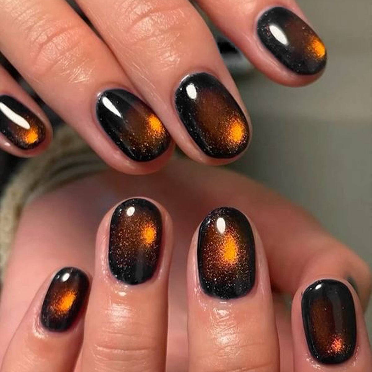 Hand wearing short glossy brown cat-eye press-on nails with orange shimmer