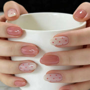 Hand wearing short round pink press-on nails with polka dots, holding a white mug