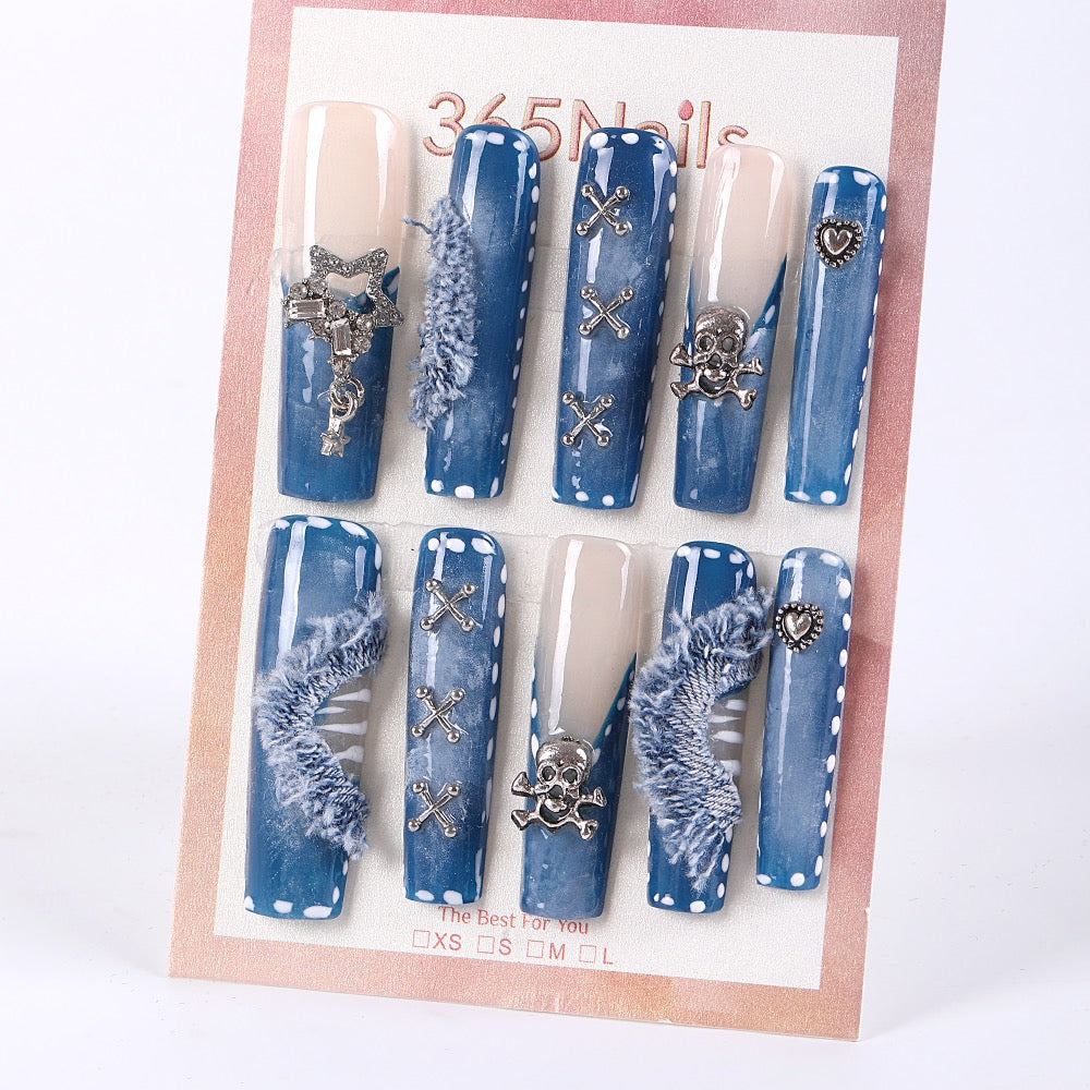 Uñas postizas largas tipo ataúd color azul denim de 365Nails con dijes de calavera y flecos afelpados.