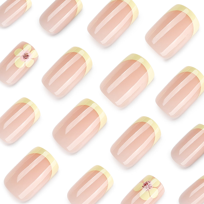 Diagonal close-up of glossy nude nails with yellow tips and floral accent