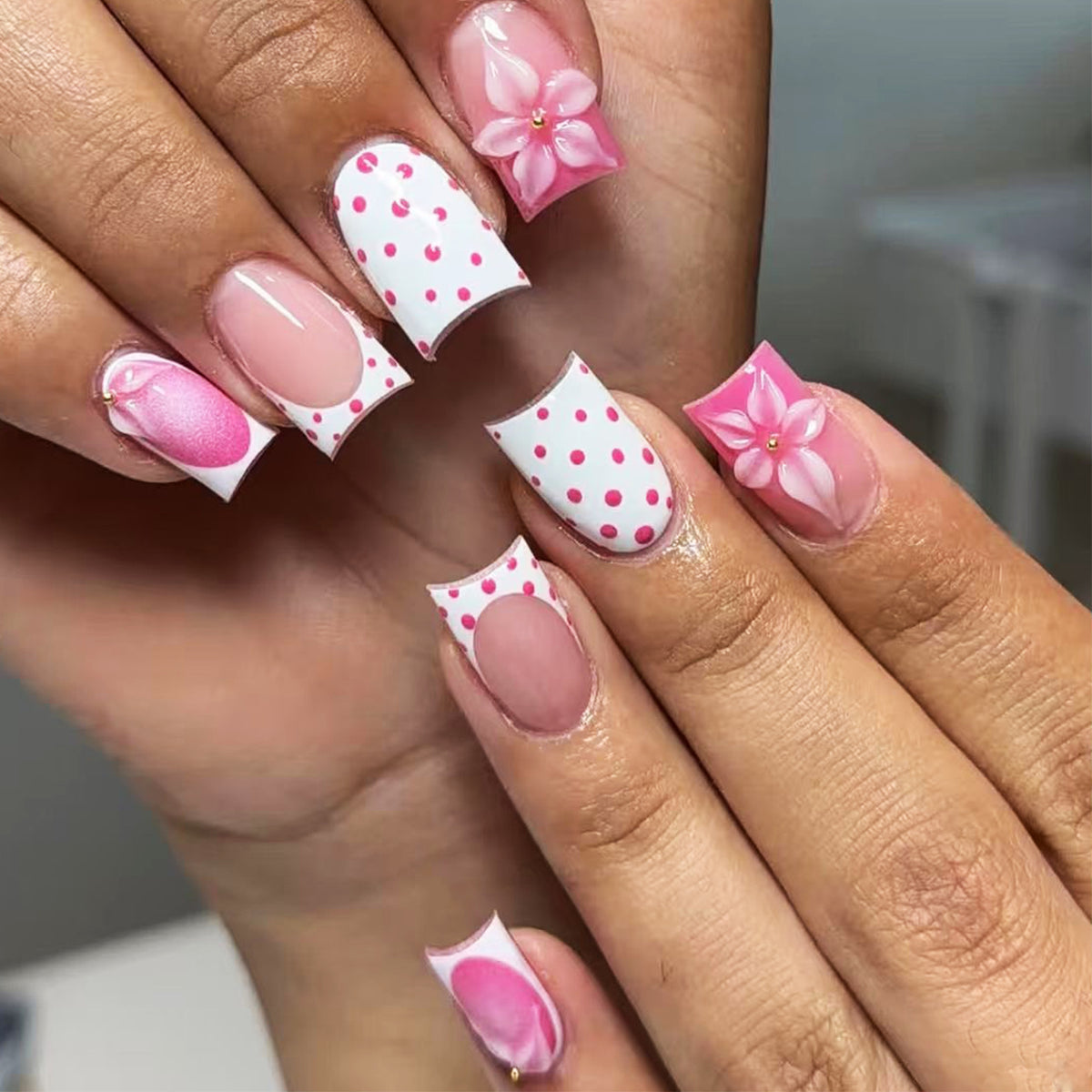 Hand wearing pink and white press-on nails with 3D flowers and polka dots