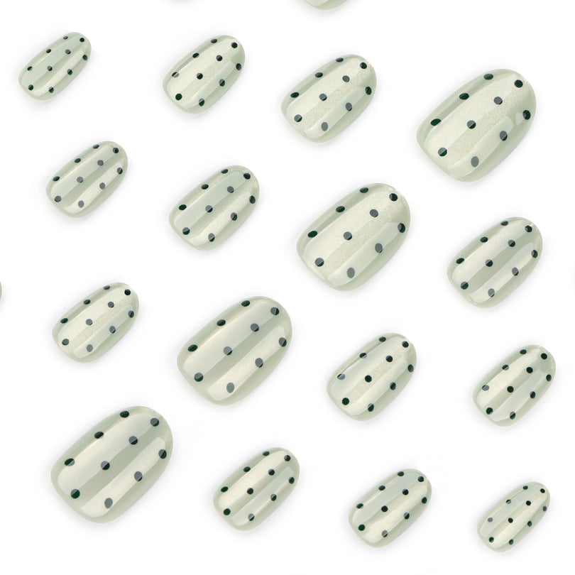 Close-up of sheer green cat-eye press-on nails with black dots