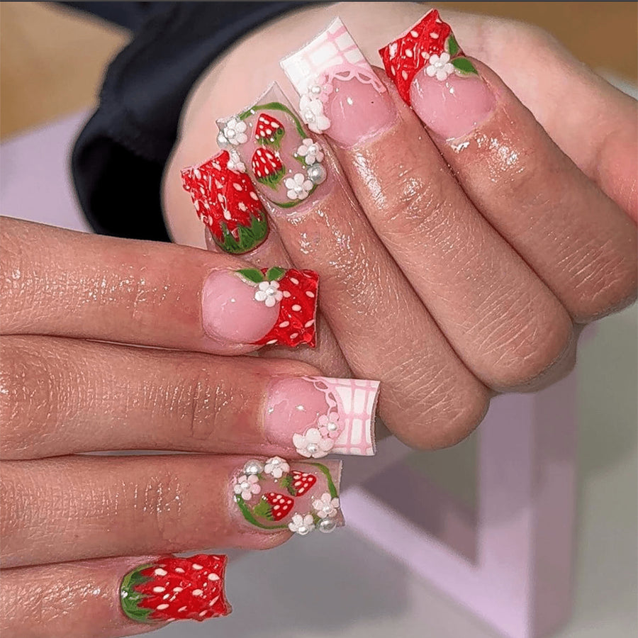 Hand wearing pink square press-on nails with 3D strawberry and lace designs