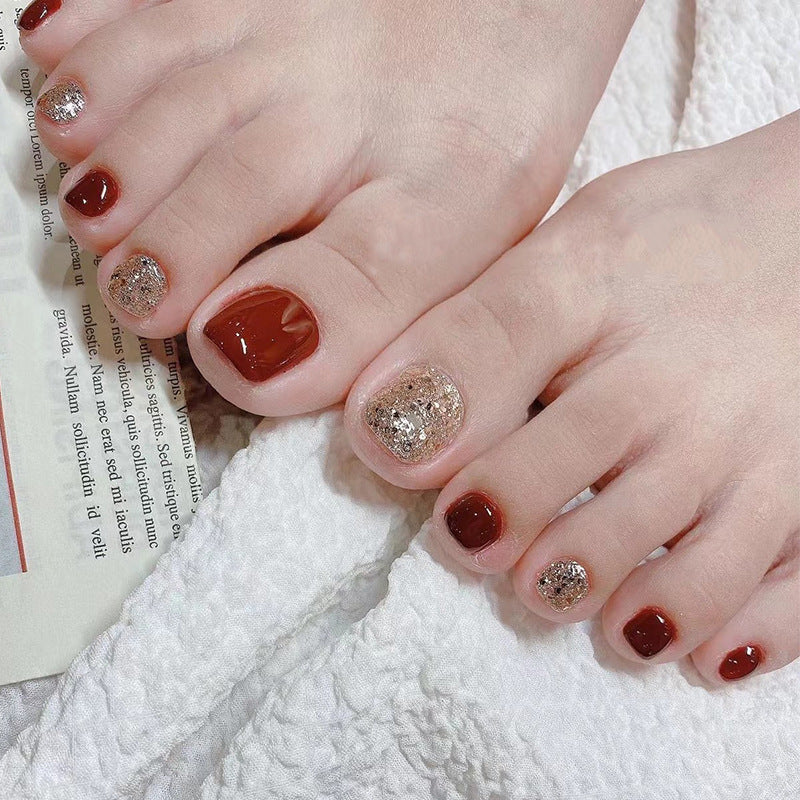 Feet wearing red and gold glitter press-on toenails on a book.