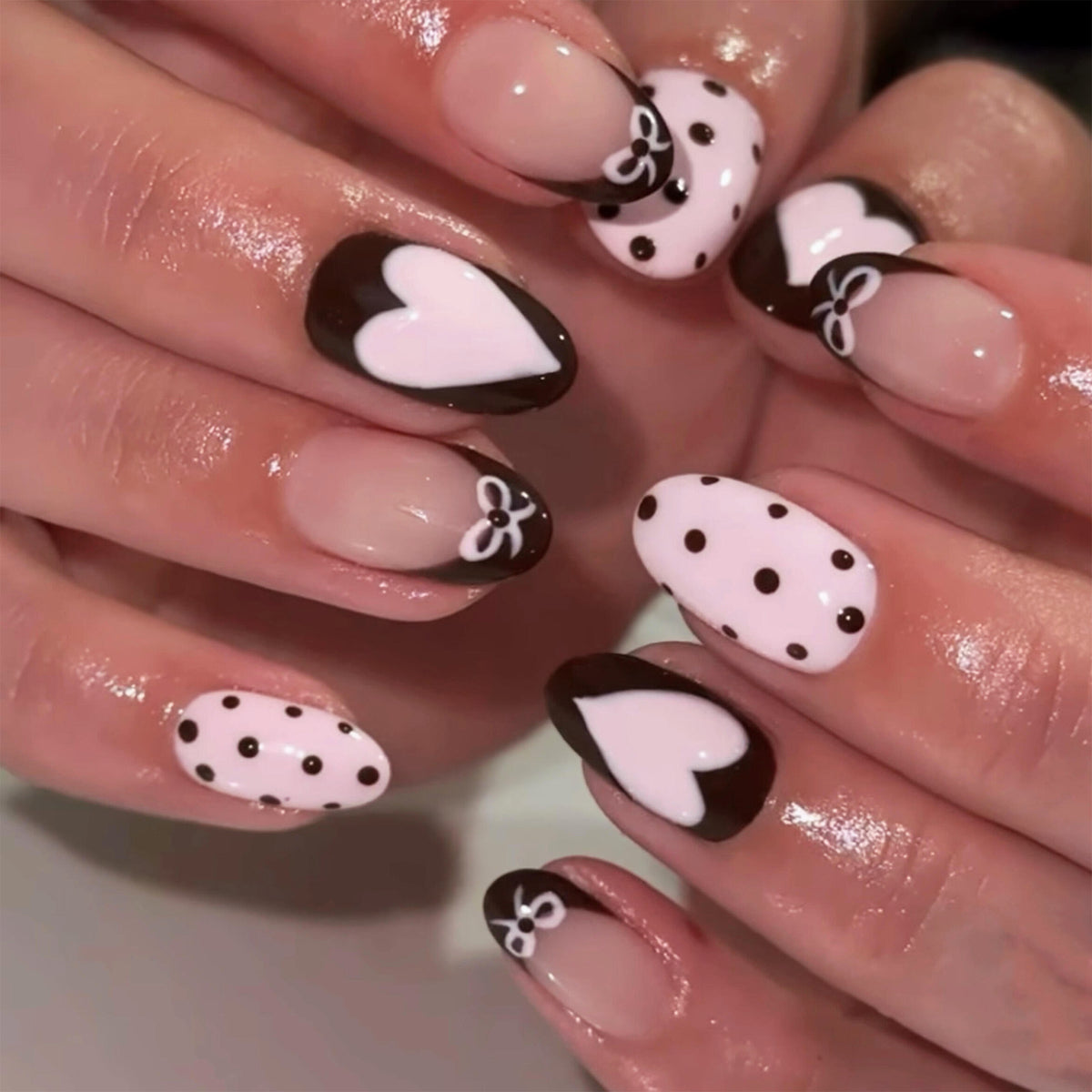 Hand wearing black and pink heart press-on nails with polka dots and bows.