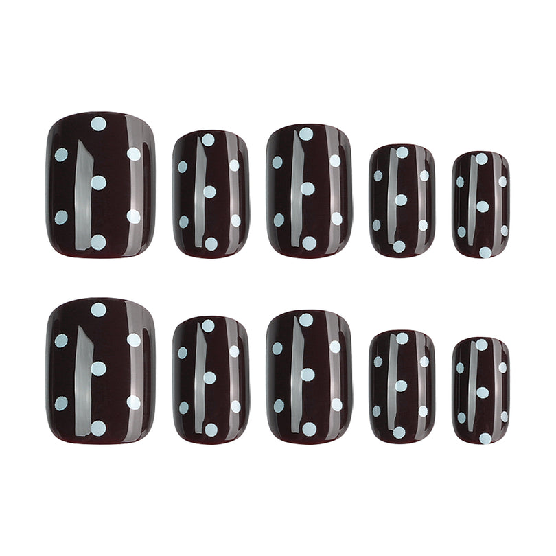 Ten black square press-on nails with white dots in two size rows