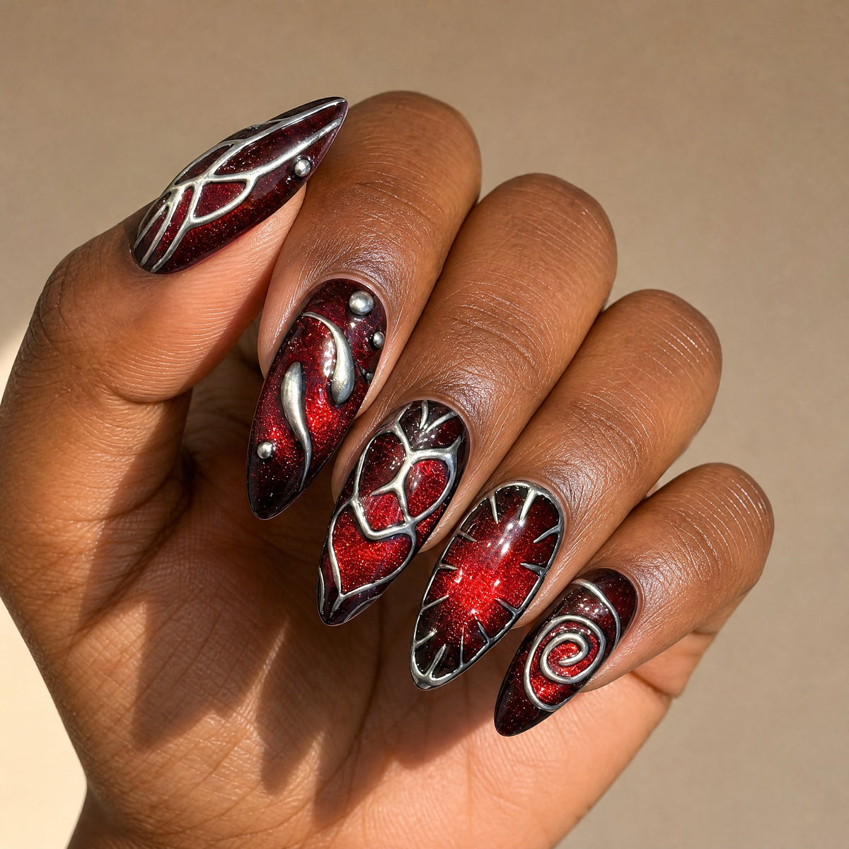 Crimson Spell 3D swirl stiletto press on nails worn on a deep skin tone hand