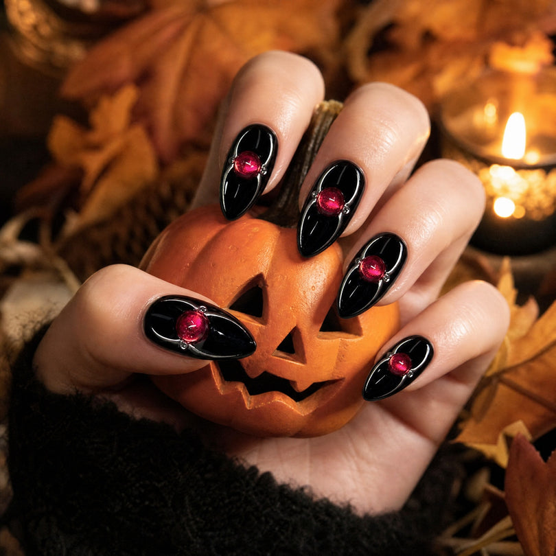 Black almond with red gem press on nails in a Halloween scene with a carved pumpkin
